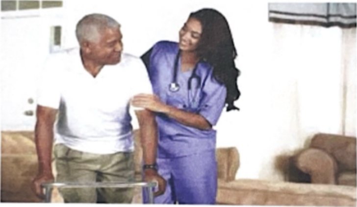 An Achievable Dreams caregiver in scrubs supporting an older adult using a walker in his living room.